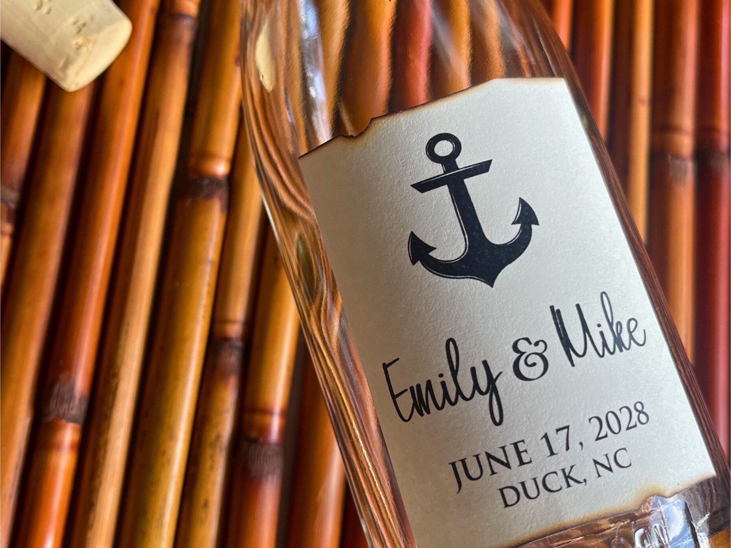 Glass bottle with a personalized label featuring an anchor design, text, and cork on a bamboo background.