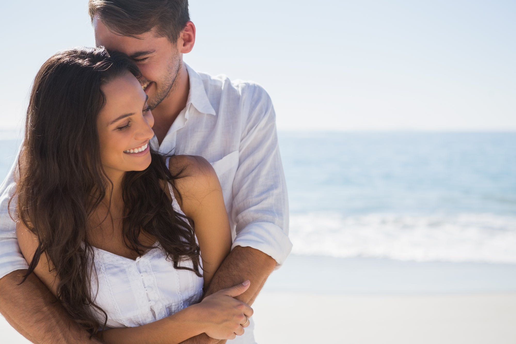Couple embracing on a beach with clear blue sky celebrating a beach wedding.