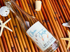 Glass bottle with a personalized wedding label on a woven mat with starfish and sand dollars.
