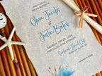 Wedding invitation with beach-themed elements on a textured surface.