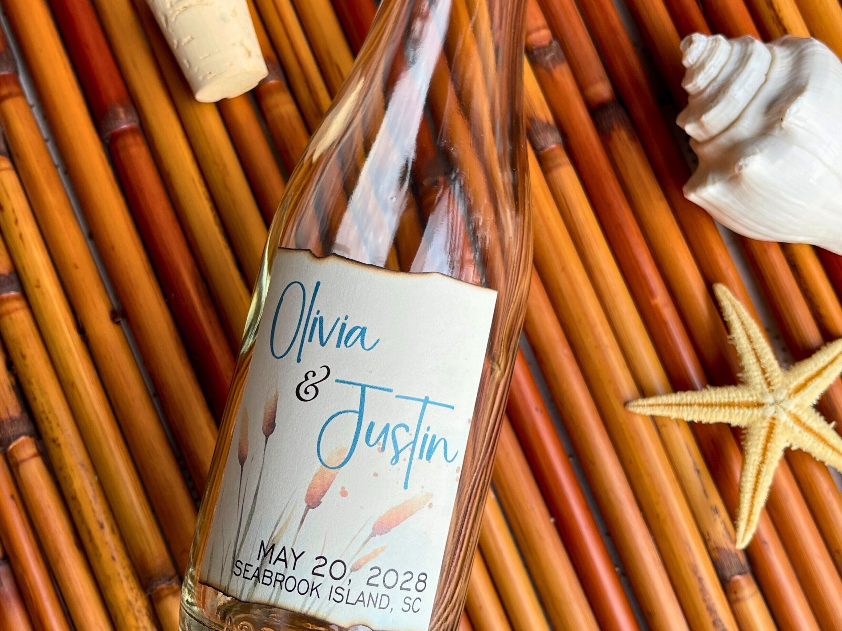 Bottle with a personalized label on a woven surface with a starfish and shell.