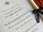 Wedding invitation with black text on a textured surface, tied with a black ribbon.