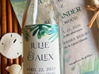 Glass bottle with tropical leaf design label and wedding invitation in the background