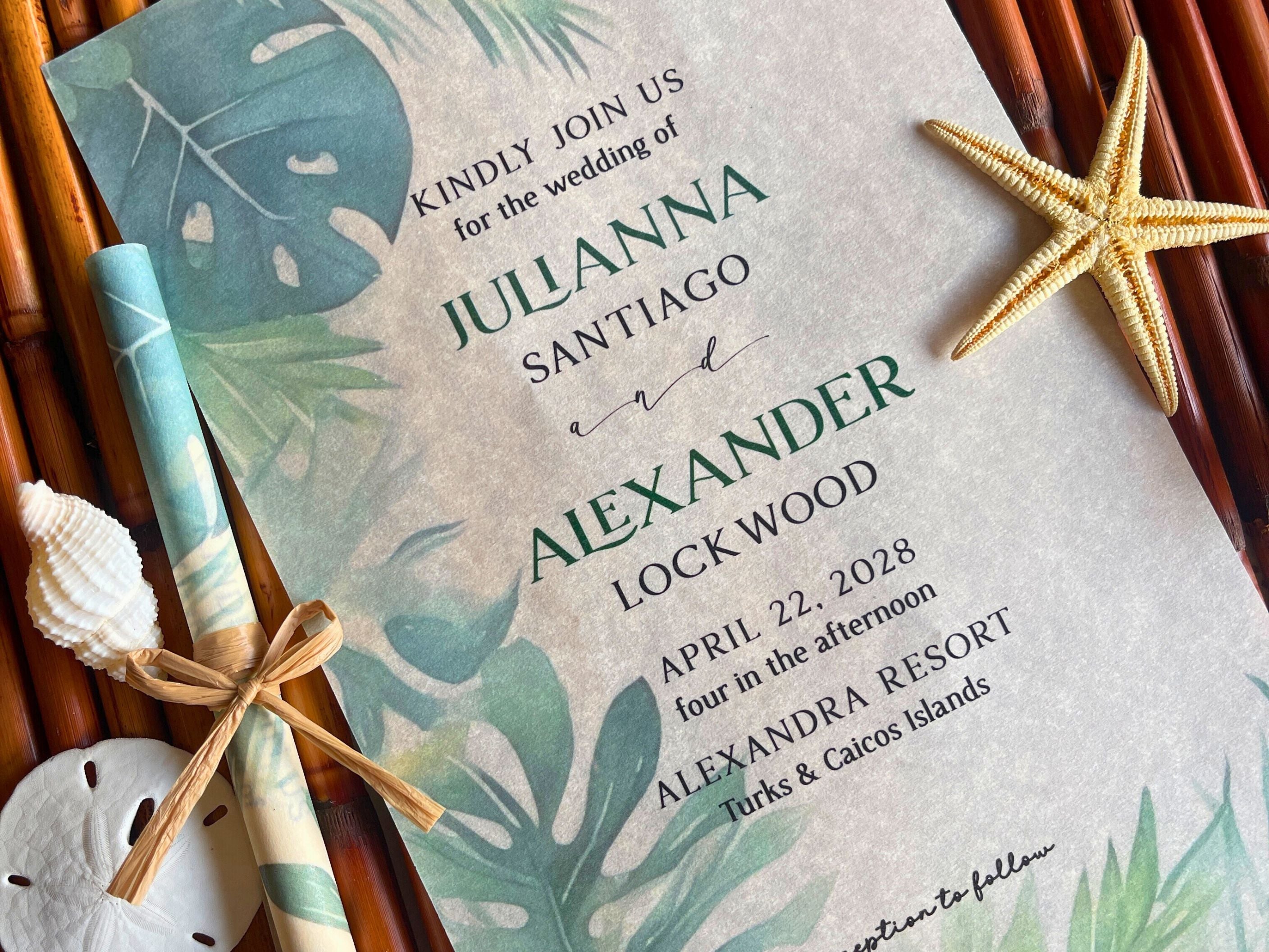 Wedding invitation with tropical leaf design, starfish, and shell on a wooden surface.