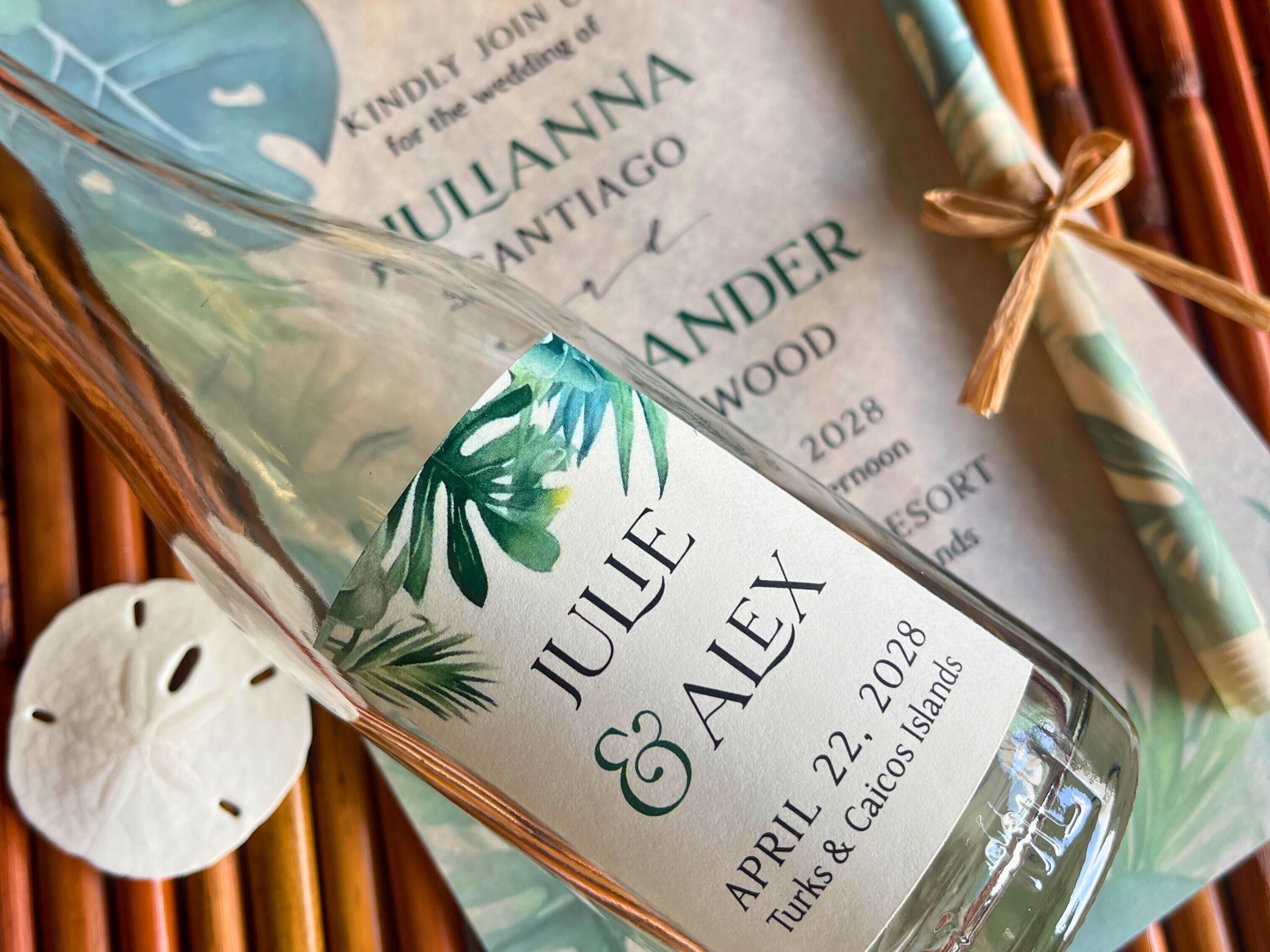 Personalized bottle label with tropical design and wedding details, placed on a woven surface.