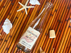 Bottle with a personalized label on a woven surface with shells and a starfish.
