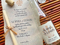 Glass bottle with personalized label and wedding invitation on a textured surface