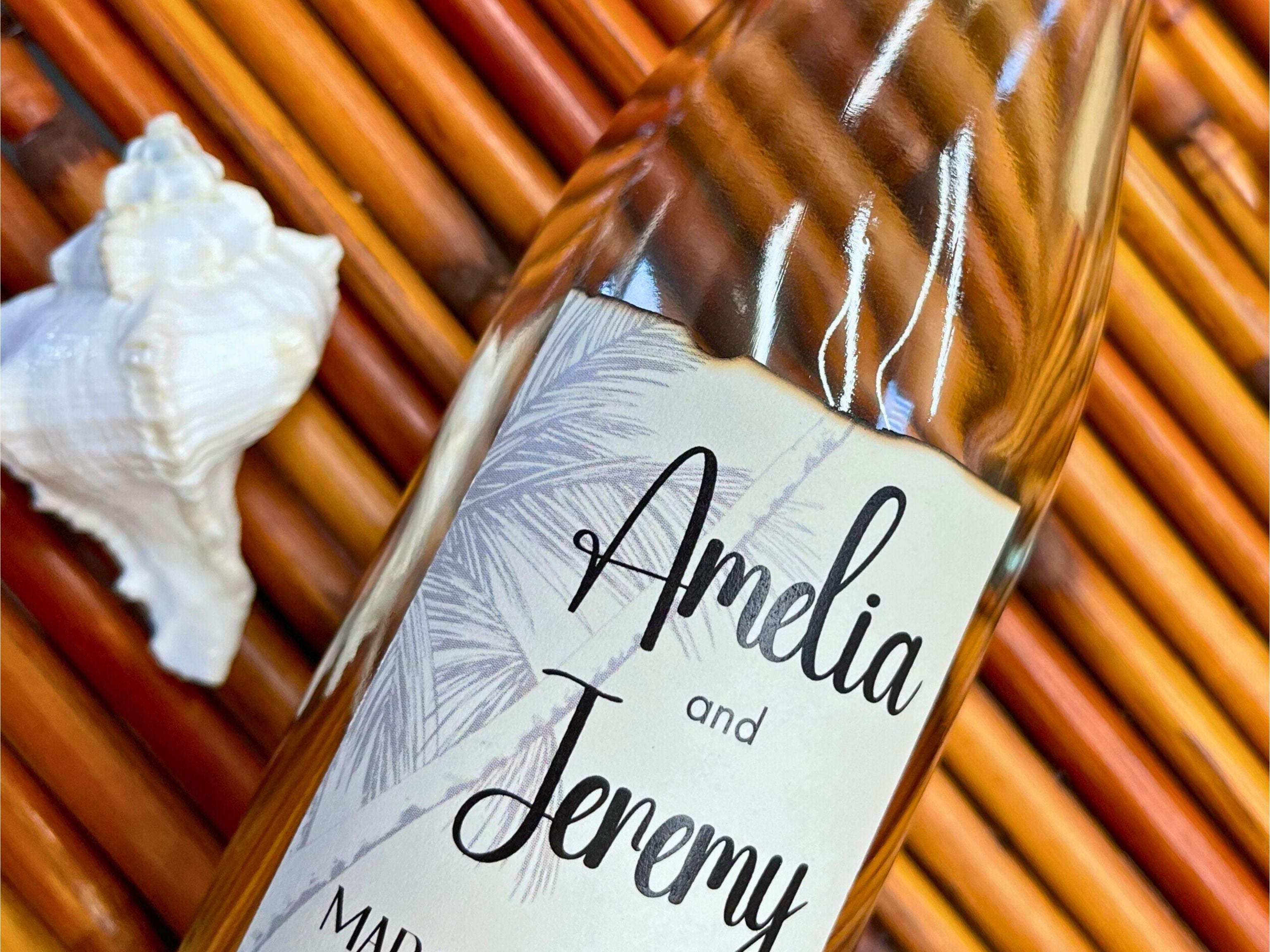 Bottle with a label reading 'Amelia and Jeremy' on a woven surface with a shell.