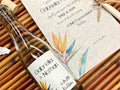Wedding invitation and glass bottle with a colorful label featuring a tropical bird of paradise plant on a woven mat